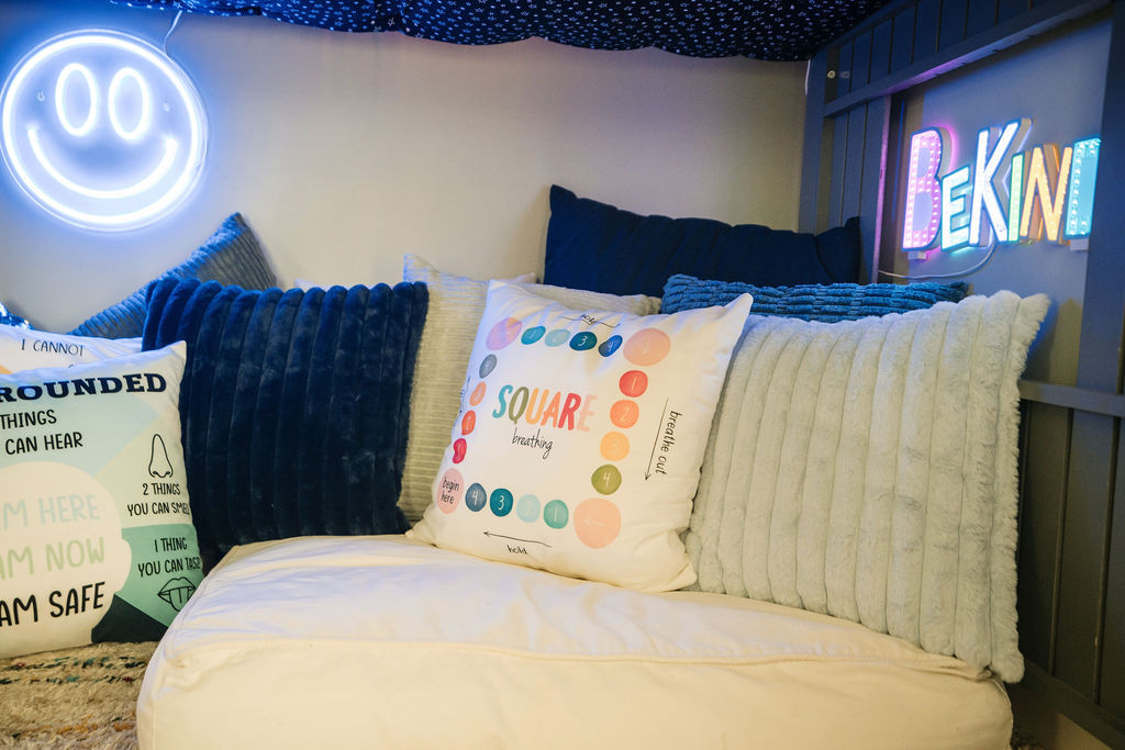 Cozy reading nook with cushions, encouraging pillows, and a neon sign